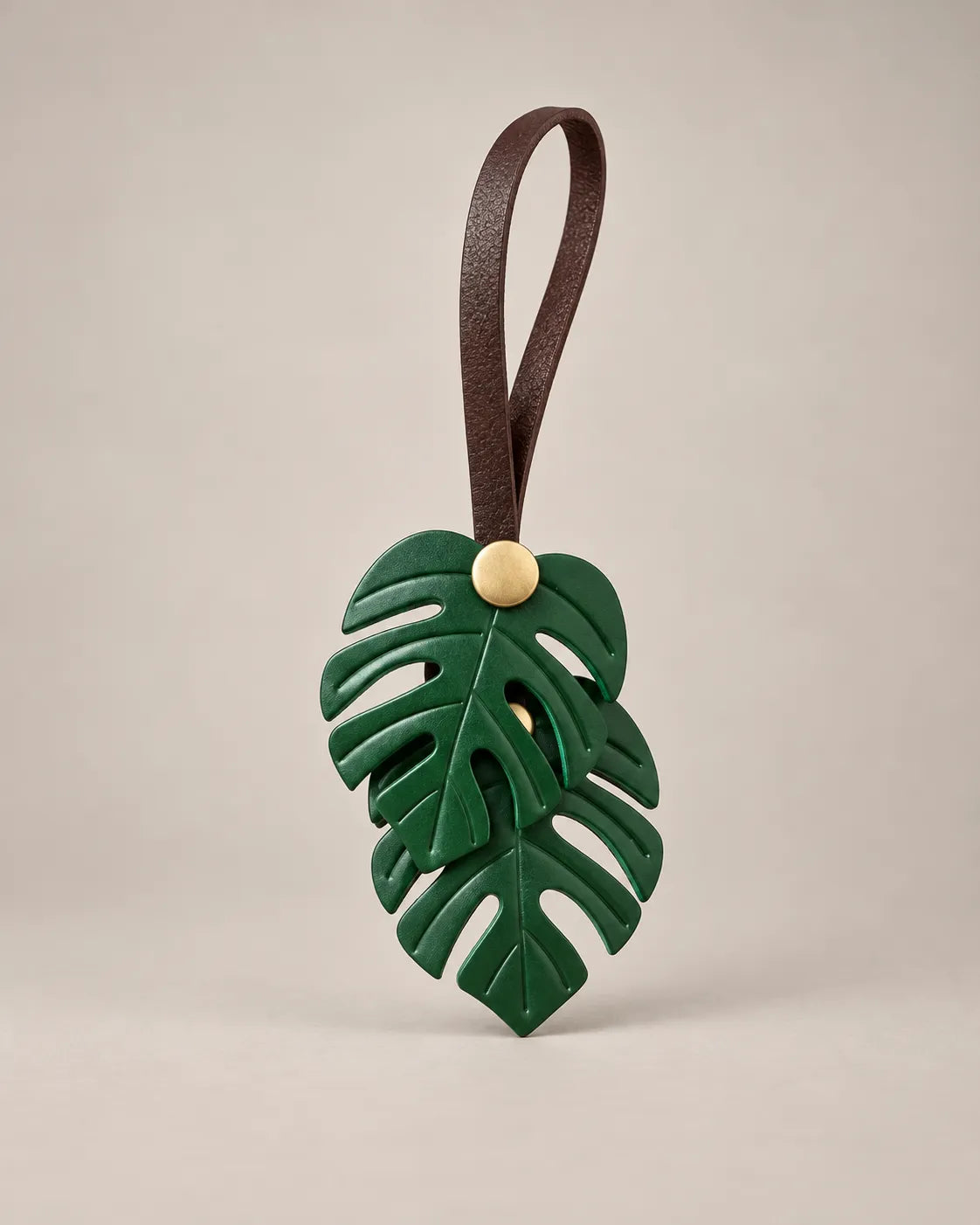 Monstera leaf bag charm in green PU leather with two leaves on a brown hanging rope and a brass-tone snap, by Malena London