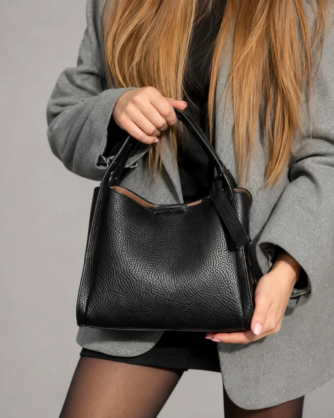 Woman holding The Amelia black genuine leather bag in a luxury studio setting. Sophisticated leather handbag for women featuring a minimalist silhouette, premium craftsmanship and refined everyday styling.