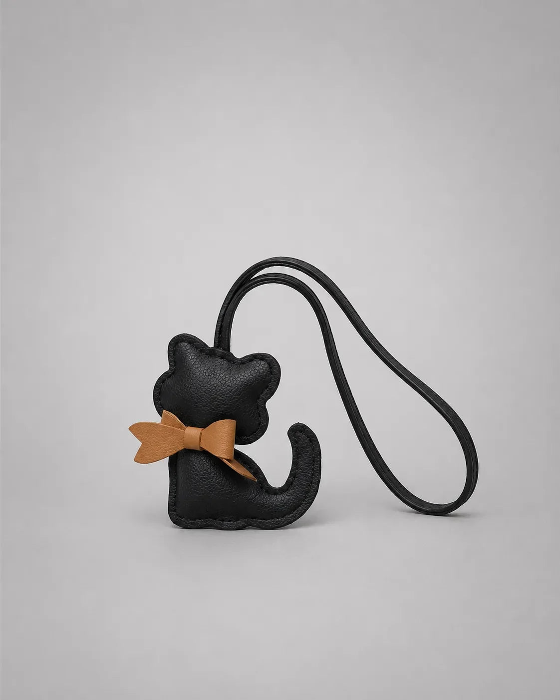 Black cat bag charm with decorative bow detail on a minimalist studio background, designed for handbag personalisation and styling.