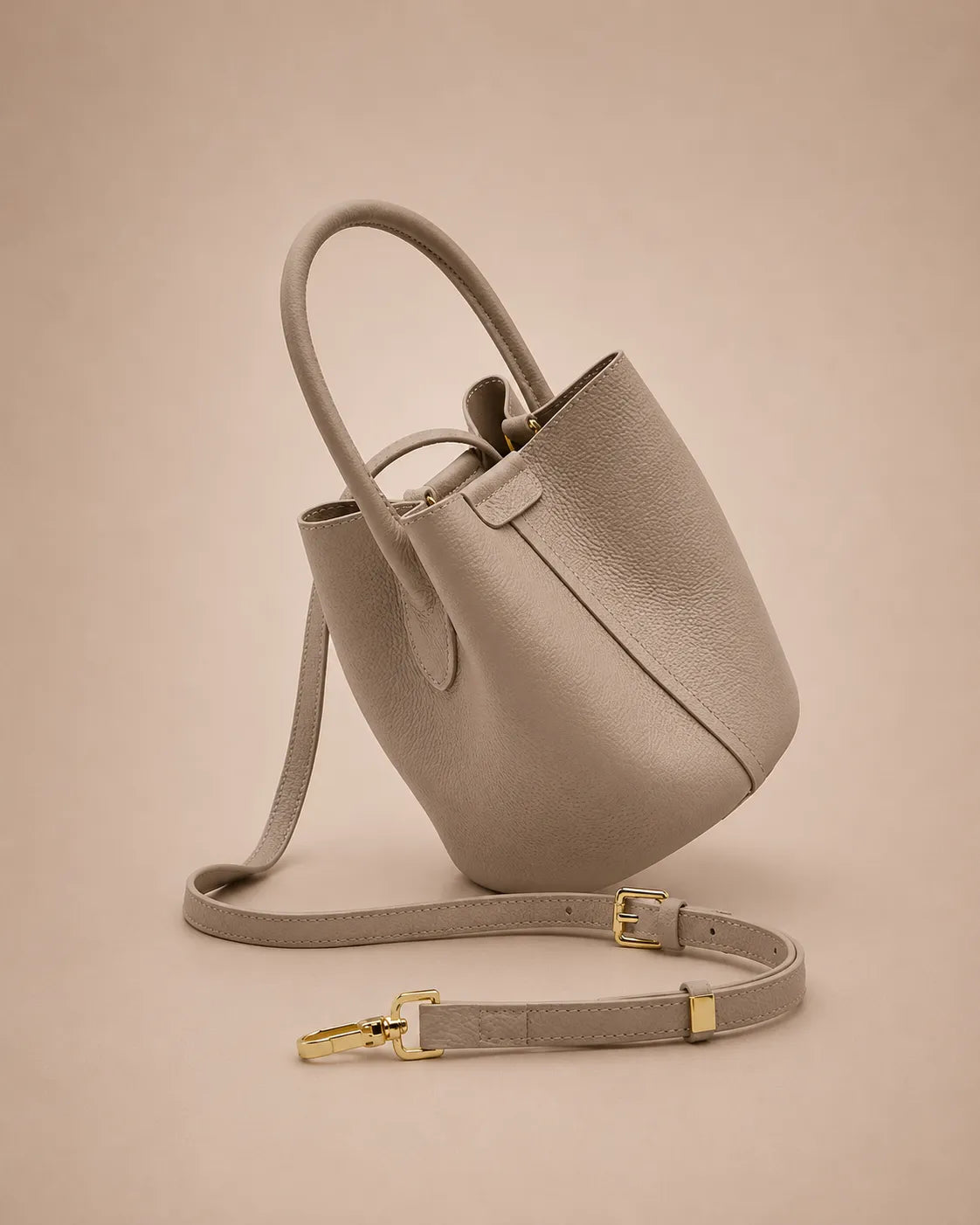 Side profile of the Charlotte leather bucket bag in elephant gray displaying its compact shape, soft structure and premium leather finish.