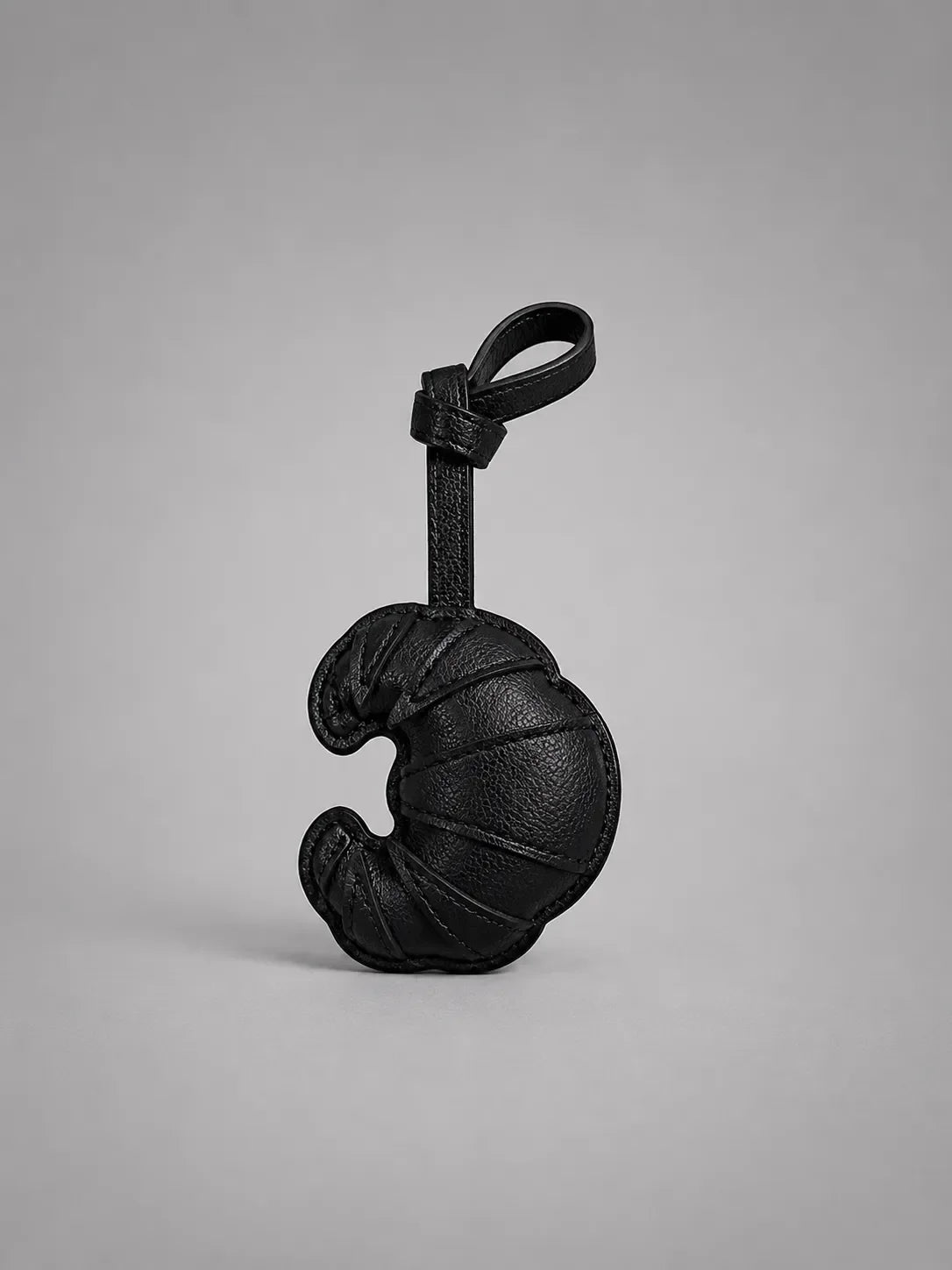 Black croissant bag charm with hanging strap, designed to personalise handbags with a playful and sophisticated detail.