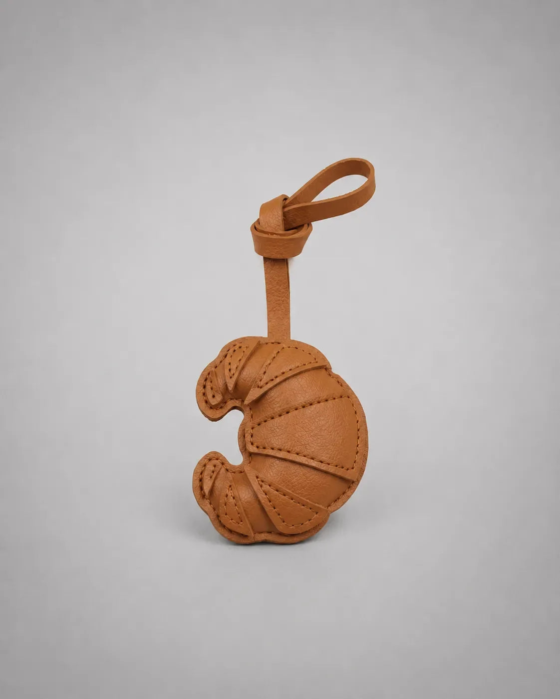 Brown croissant bag charm with hanging strap, inspired by French pastry design and crafted as a stylish handbag accessory.