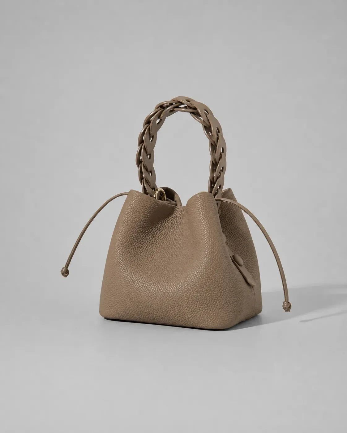 Front angled view of the Léonie genuine leather bucket bag in Cookie featuring a sculptural braided leather top handle, drawstring closure, soft structured silhouette and premium craftsmanship designed for statement day-to-evening styling by Malena London.