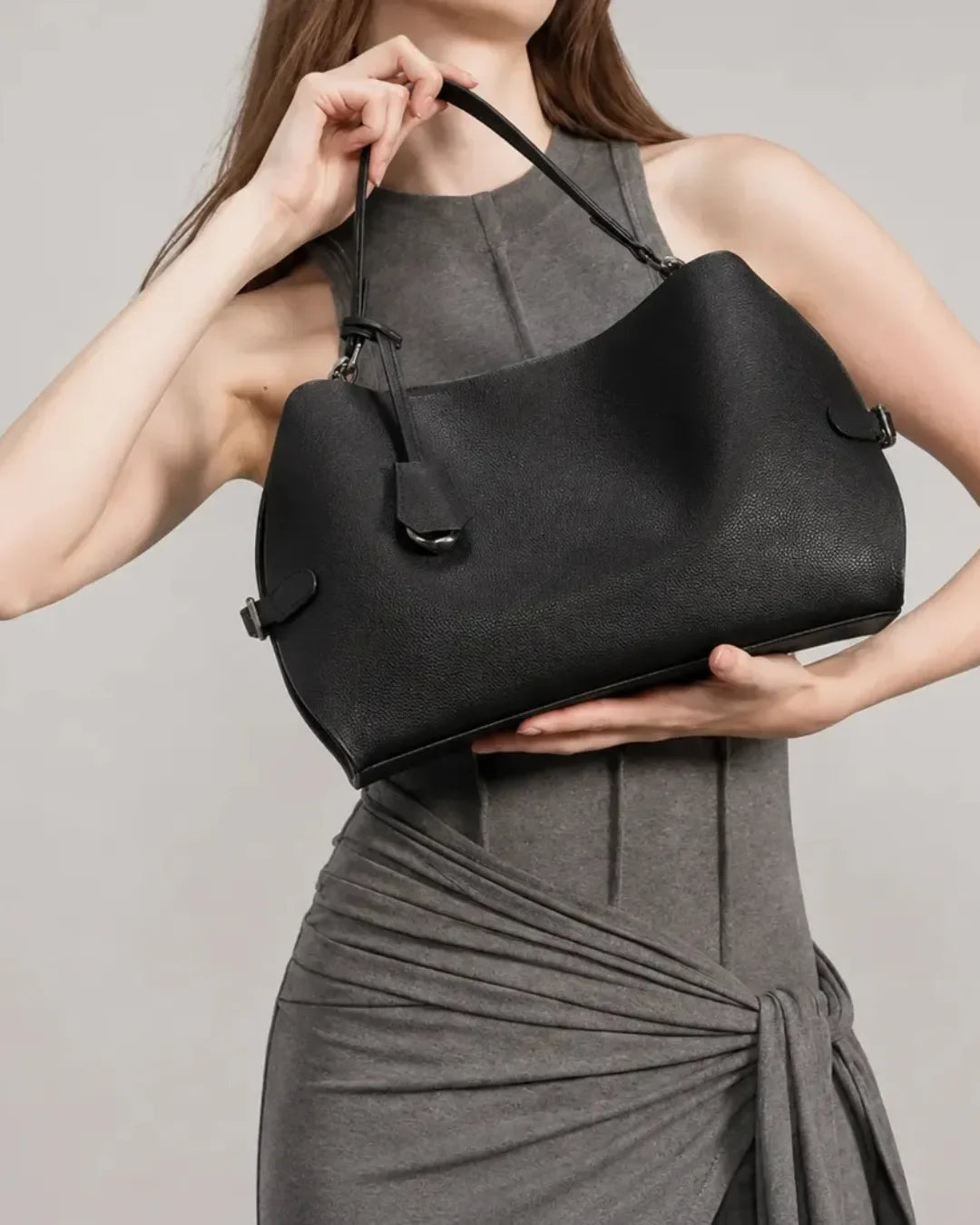 Woman holding the black The Eliza genuine leather shoulder bag close to the body, showcasing the softly structured silhouette, premium leather texture and elegant everyday design.