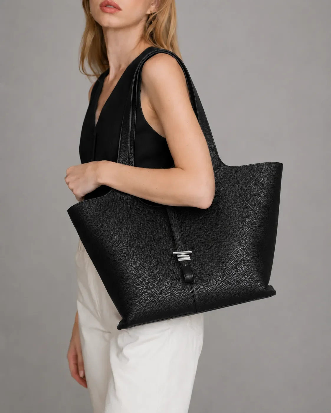 Woman carrying the Victoria genuine leather tote bag in Black. Elegant women's leather tote featuring a spacious silhouette, premium pebbled leather and comfortable shoulder straps for work, commuting and everyday use.