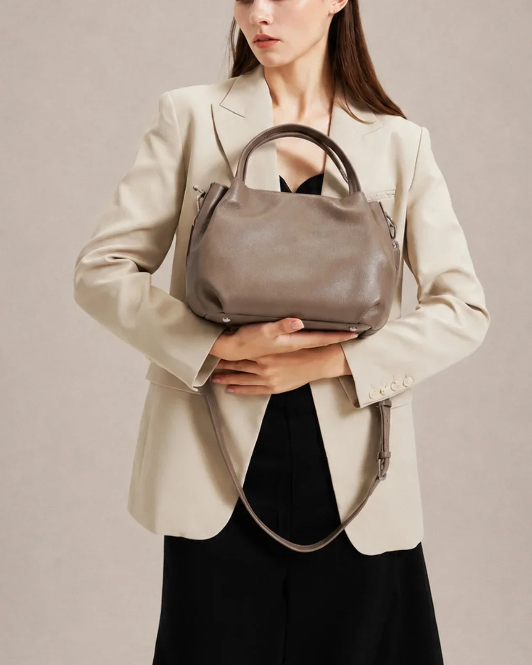 Woman holding the Pauline genuine leather top handle crossbody bag in Taupe, showcasing its elegant silhouette and refined day-to-evening styling by Malena London.