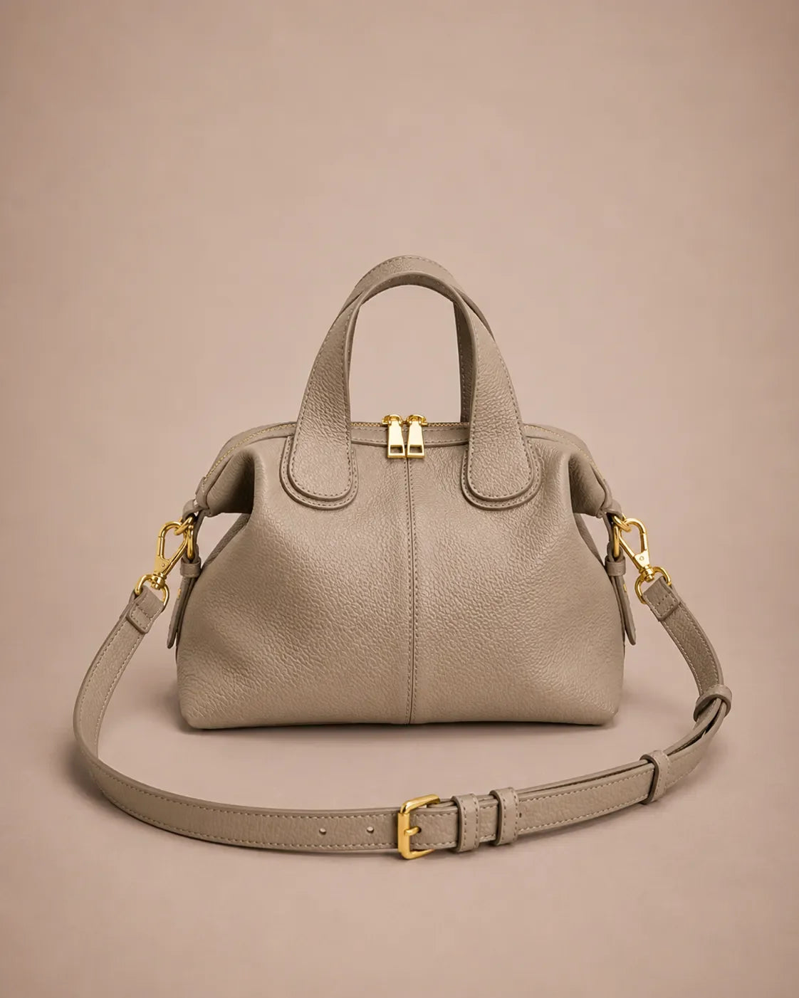 Victoire leather dumpling bag in Elephant Gray genuine leather featuring a soft structured silhouette, double top handles, adjustable shoulder strap, gold-tone hardware and zip closure, photographed from the front on the Malena London studio beige background.