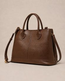 Angled view of the Odile large structured genuine leather tote bag in brown showing the panelled silhouette and gold-tone hardware.