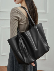 Woman wearing the Rosalind oversized genuine leather tote bag in black on the shoulder, close view.