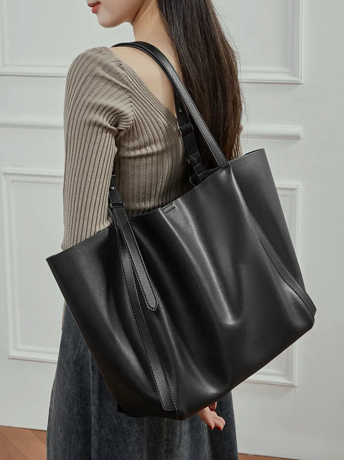 Woman wearing the Rosalind oversized genuine leather tote bag in black on the shoulder, close view.