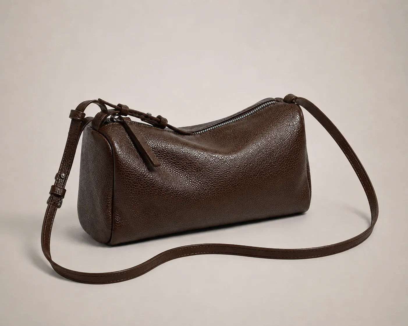 Angled view of the Simone genuine leather cylindrical crossbody bag in brown showing the zip closure and stitching detail.