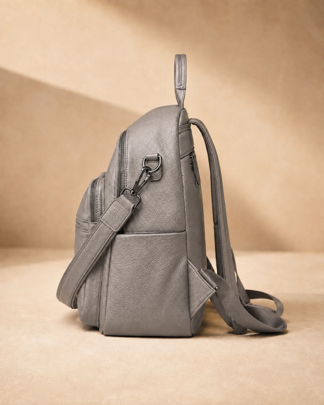 Side view of the Isla lightweight genuine leather travel backpack in grey showing the zip pocket and top handle