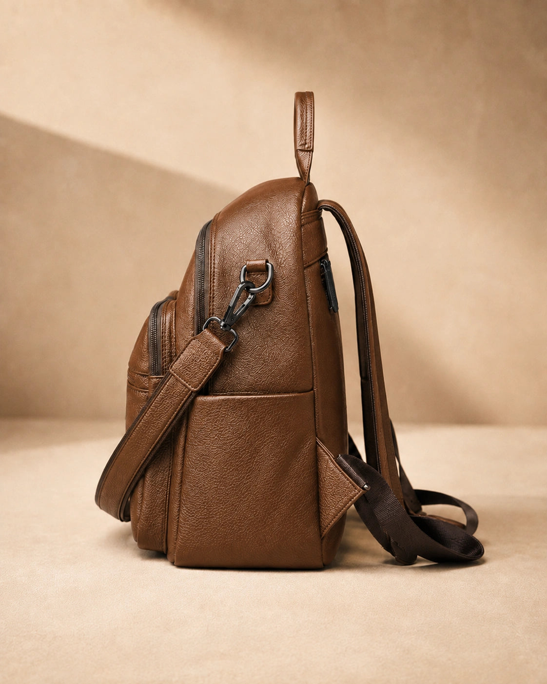 Side view of the Isla lightweight genuine leather travel backpack in brown showing the zip pocket and top handle