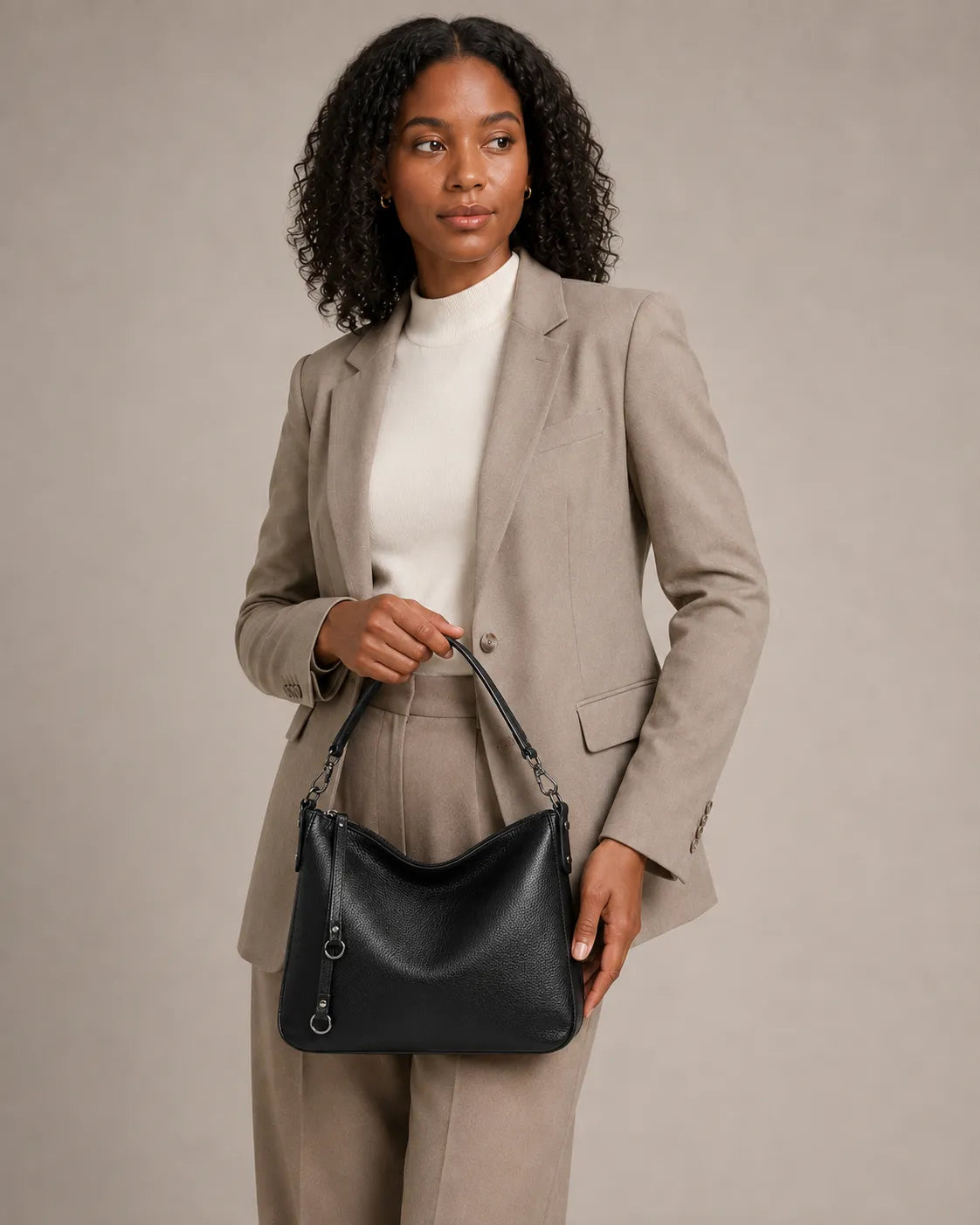 Woman holding the Noémie soft genuine leather hobo shoulder bag in black by the top handle.