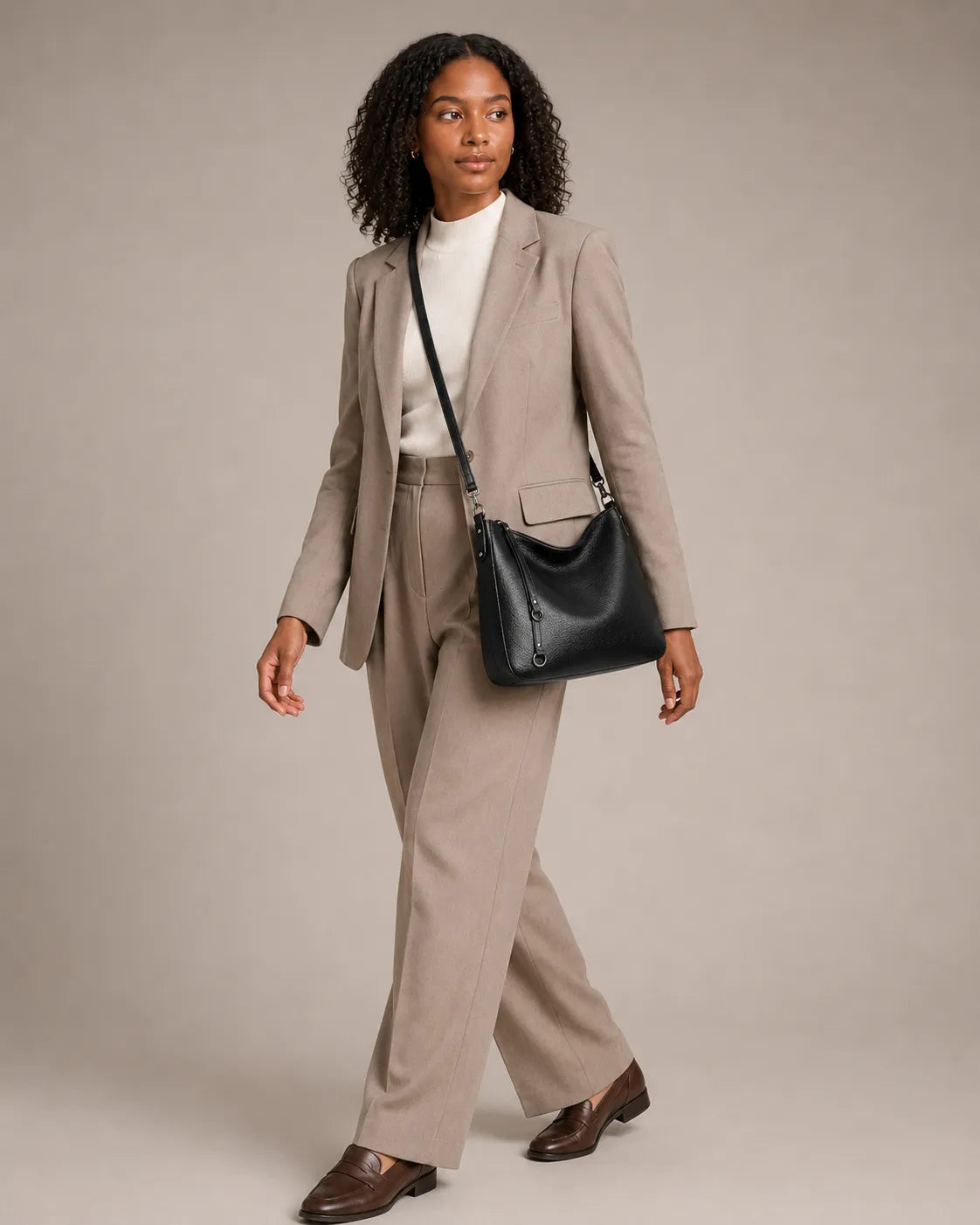 Woman wearing the Noémie soft genuine leather hobo shoulder bag in black on the shoulder while walking.