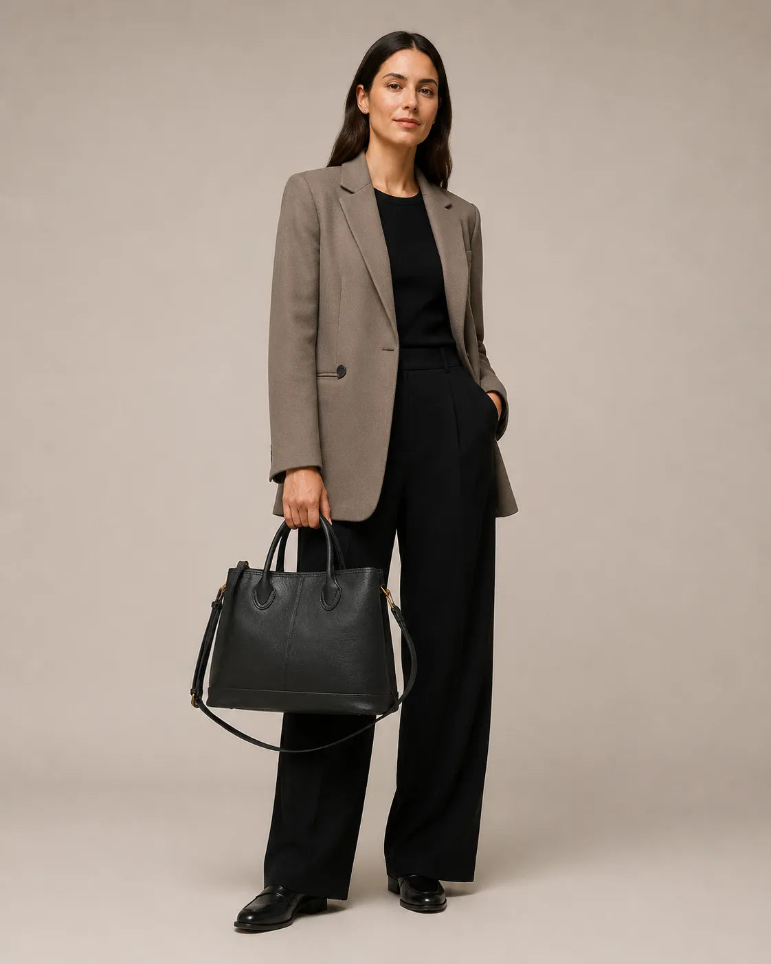 Woman standing with the Odile large structured genuine leather tote bag in black held by the top handles.