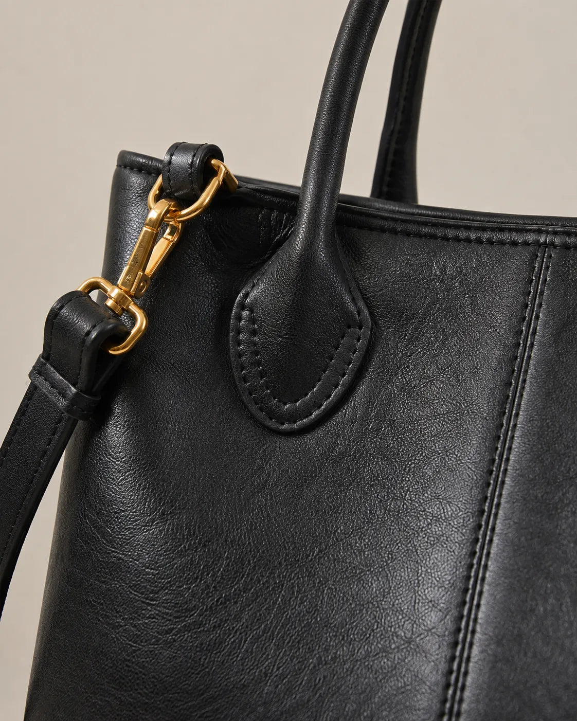 Close-up detail of the Odile large structured genuine leather tote bag in black showing the gold-tone hardware and stitching.