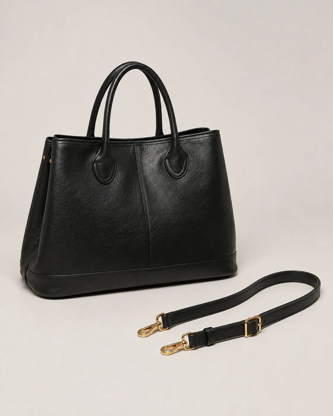 Angled view of the Odile large structured genuine leather tote bag in black with the crossbody strap laid out.