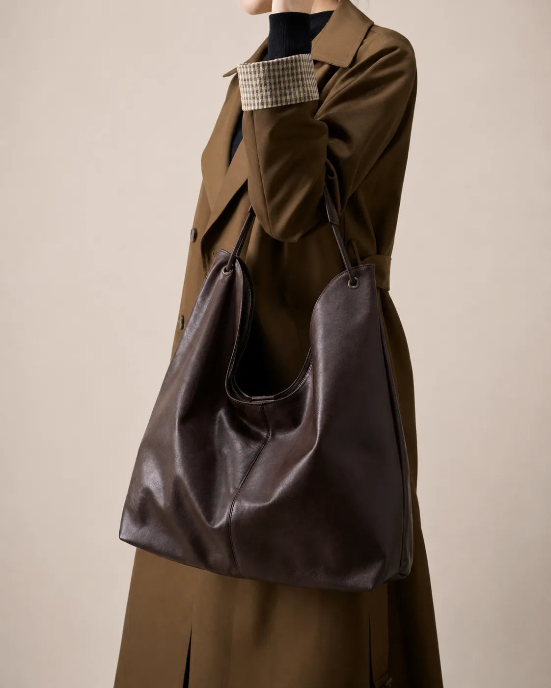 Close-up lifestyle view of the Colette dark chocolate leather hobo tote bag styled with a tailored trench coat, highlighting its soft structure and relaxed silhouette.