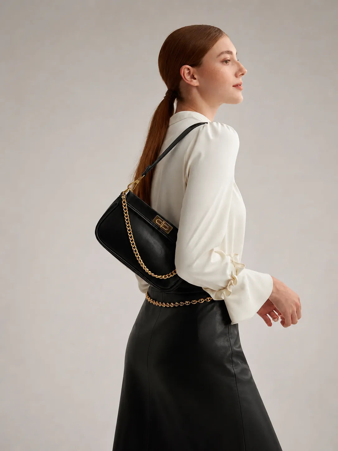 Woman carrying a black leather shoulder bag with gold chain detail from the Day to Evening Leather Bags collection by Malena London.