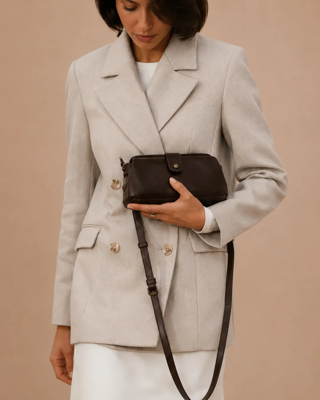 Model holding the Eloise leather crossbody bag in dark chocolate genuine leather, styled with a tailored blazer and boots.