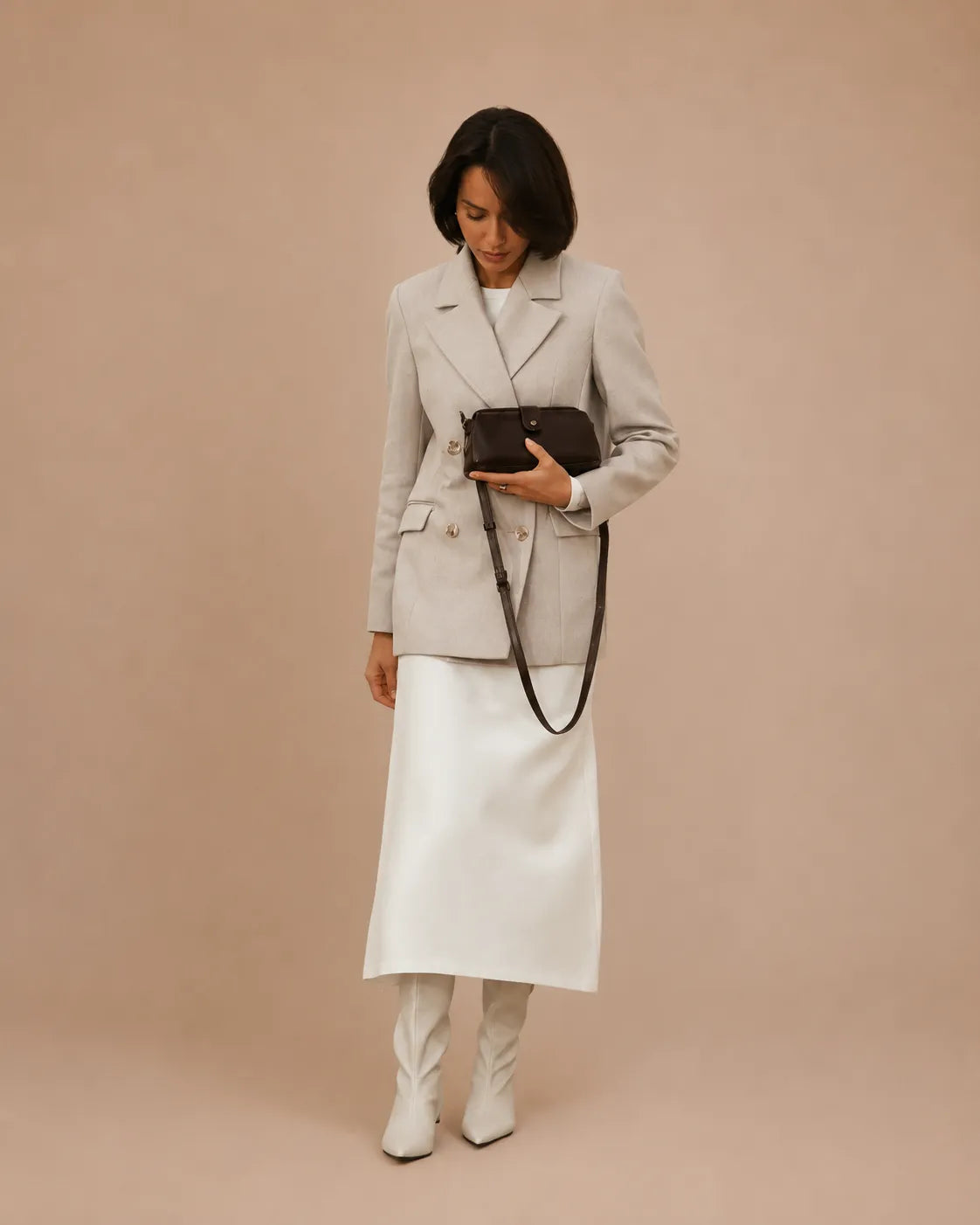 Model holding the Eloise leather crossbody bag in dark chocolate genuine leather, styled with a tailored blazer and boots.