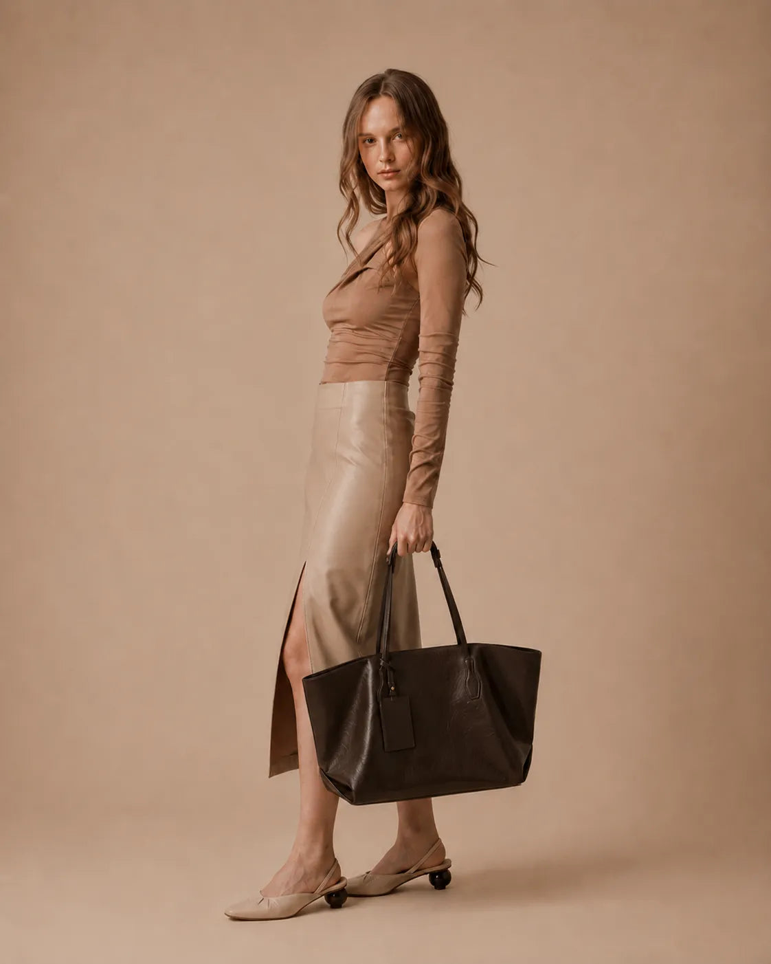 Woman wearing the Emilia Tote in dark chocolate leather, demonstrating its spacious design and refined soft structure silhouette.