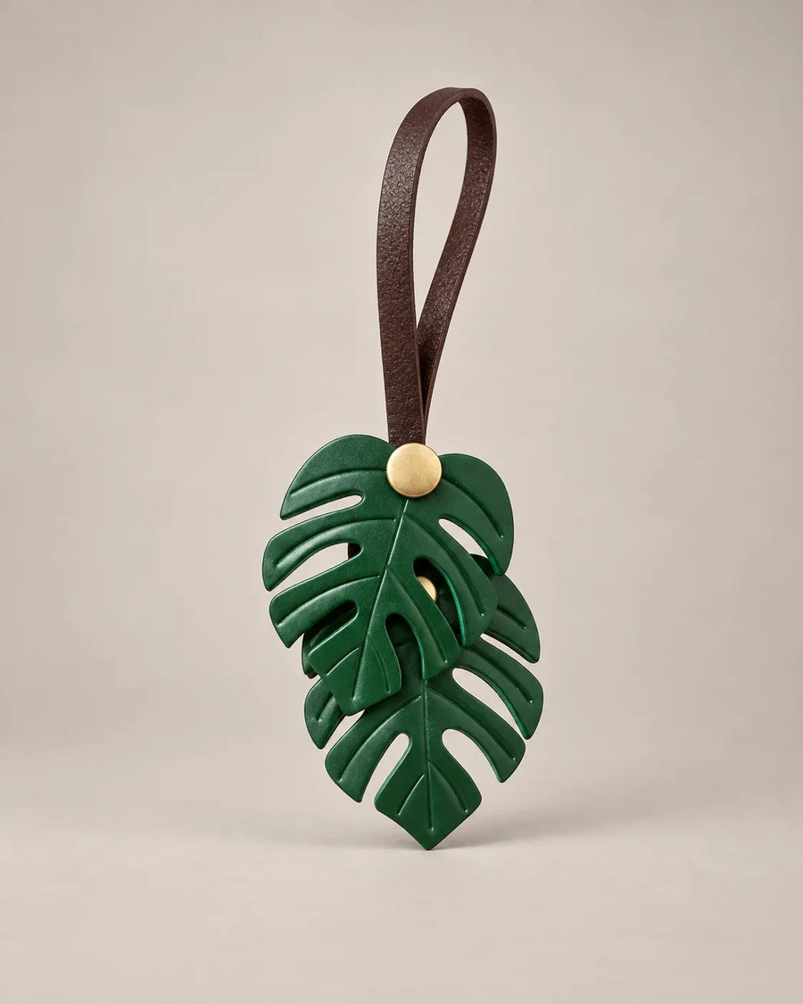 Monstera leaf bag charm in green PU leather with two leaves on a brown hanging rope and a brass-tone snap, by Malena London