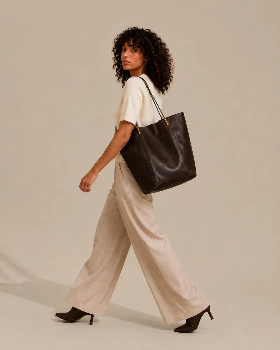Woman carrying the Margot Tote in dark chocolate genuine leather, showcasing its elegant silhouette and spacious everyday design.