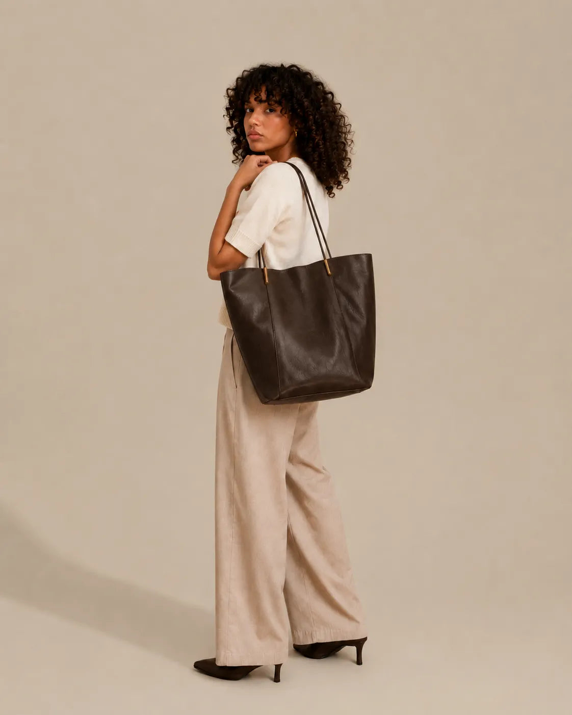Woman carrying the Margot Tote over the shoulder in dark chocolate genuine leather, highlighting its versatile and timeless design.