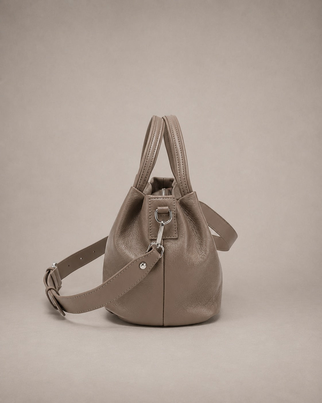Side view of the Pauline genuine leather top handle crossbody bag in taupe showing the elegant profile, adjustable crossbody strap and softly structured design by Malena London.