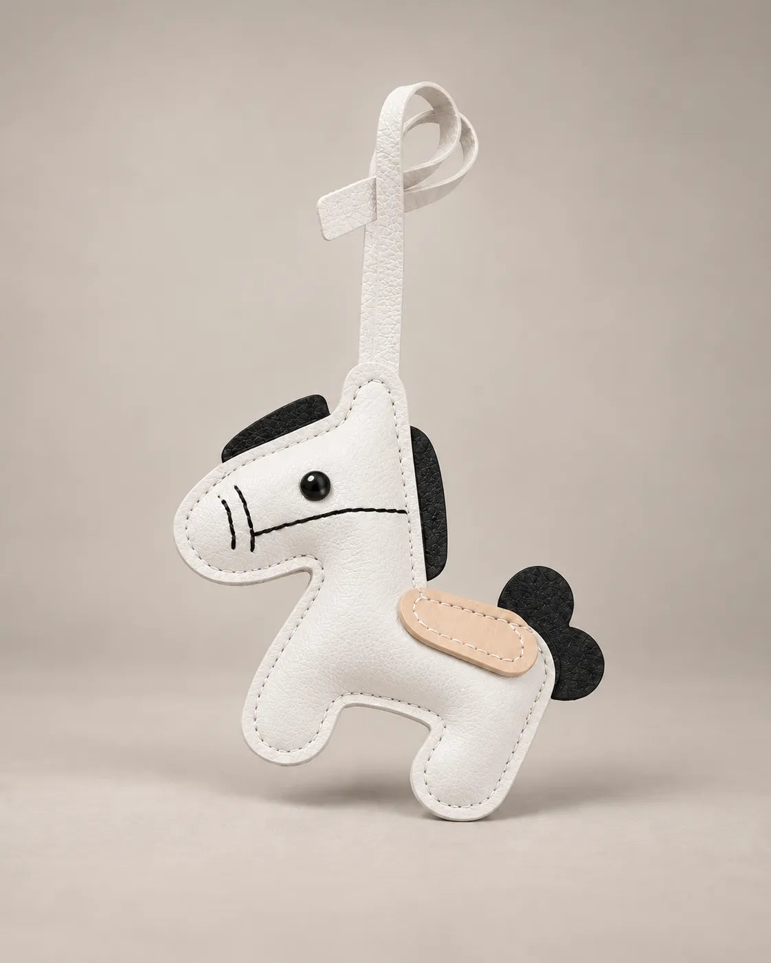 Pony bag charm in white PU leather with a black mane and tail, tan saddle patch and a hanging strap, by Malena London