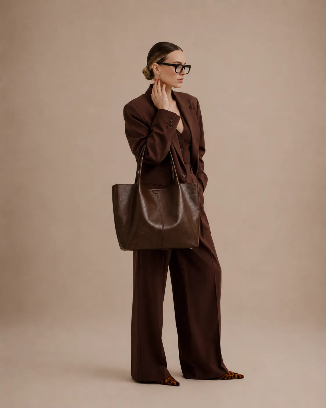 Woman styling the Valentina Tote in dark chocolate leather with a tailored workwear outfit, showcasing its spacious design and refined aesthetic.