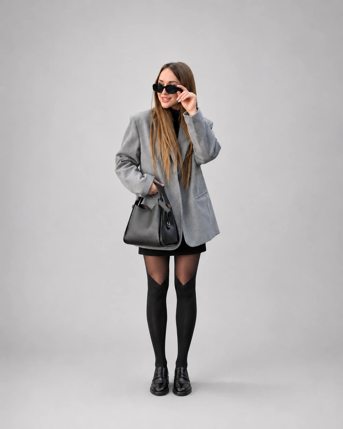 Woman wearing The Amelia black genuine leather handbag styled with a tailored grey blazer and loafers. Structured leather bag for women combining timeless elegance, everyday functionality and contemporary city style.
