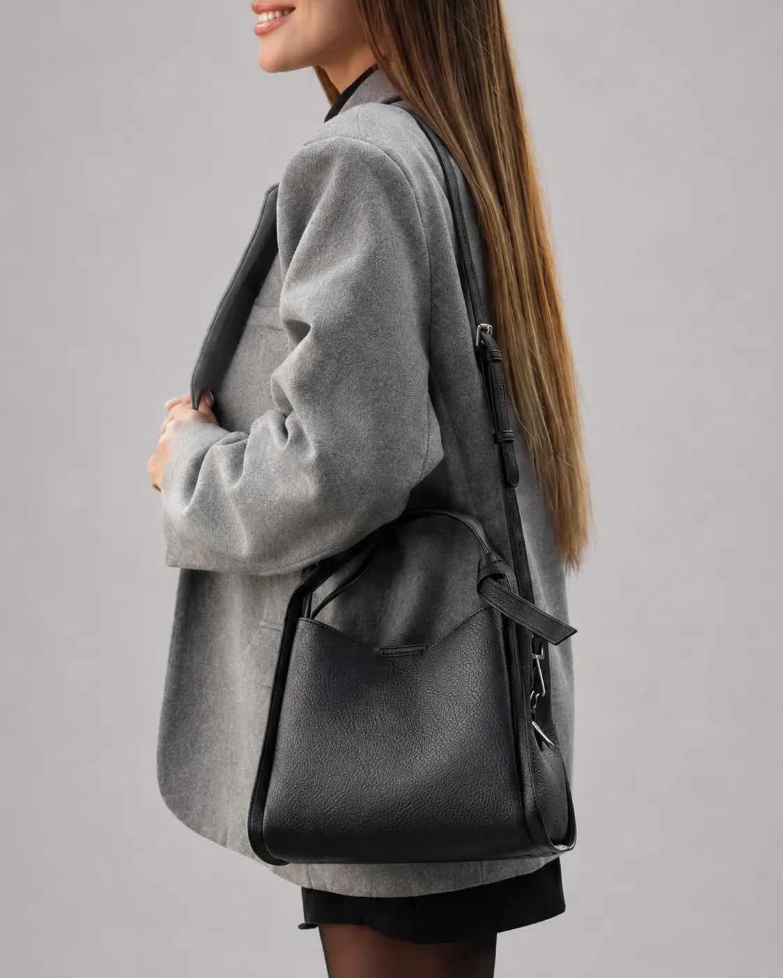 Woman carrying The Amelia black genuine leather handbag over the shoulder, styled with a grey blazer and black outfit. Elegant women's leather handbag designed for everyday wear, city style and modern versatility.