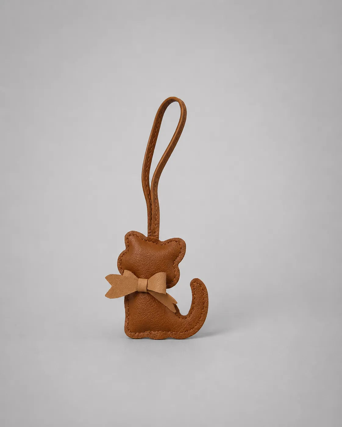 Brown cat bag charm featuring a bow accent and hanging loop, displayed on a neutral studio background for handbag styling.