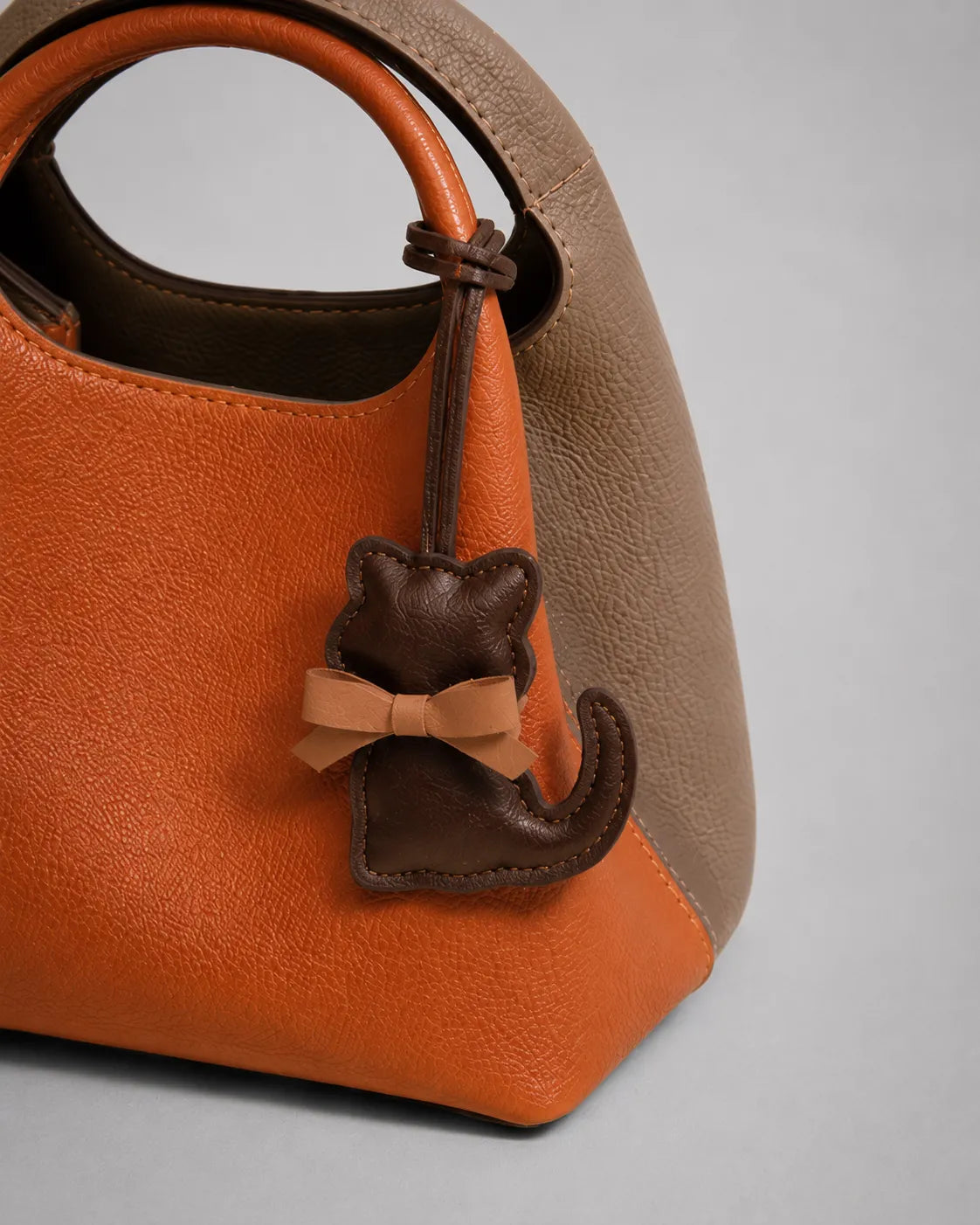 Dark chocolate cat bag charm with bow detail attached to a structured handbag, shown in a close-up view highlighting styling and handbag personalisation.