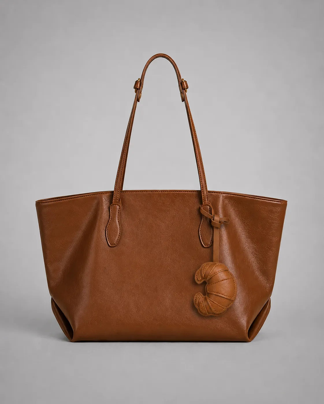 Brown croissant bag charm styled on a tote bag, adding a playful and elegant touch to everyday handbag accessories.
