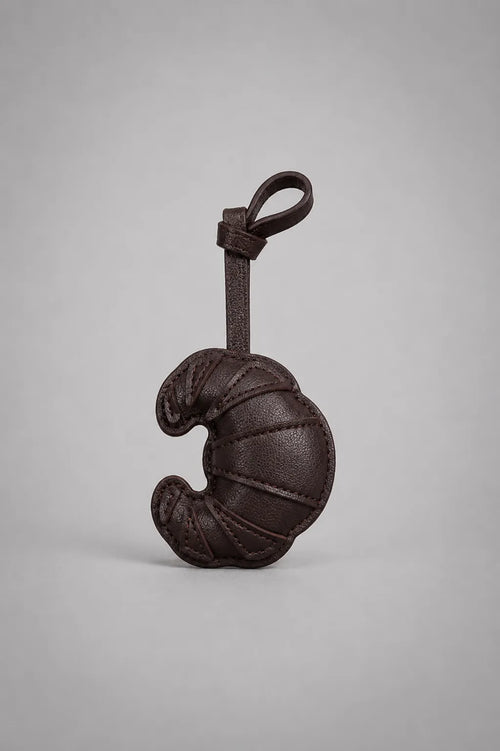 Dark chocolate croissant bag charm with hanging strap, designed as a unique handbag accessory inspired by classic French pastries.