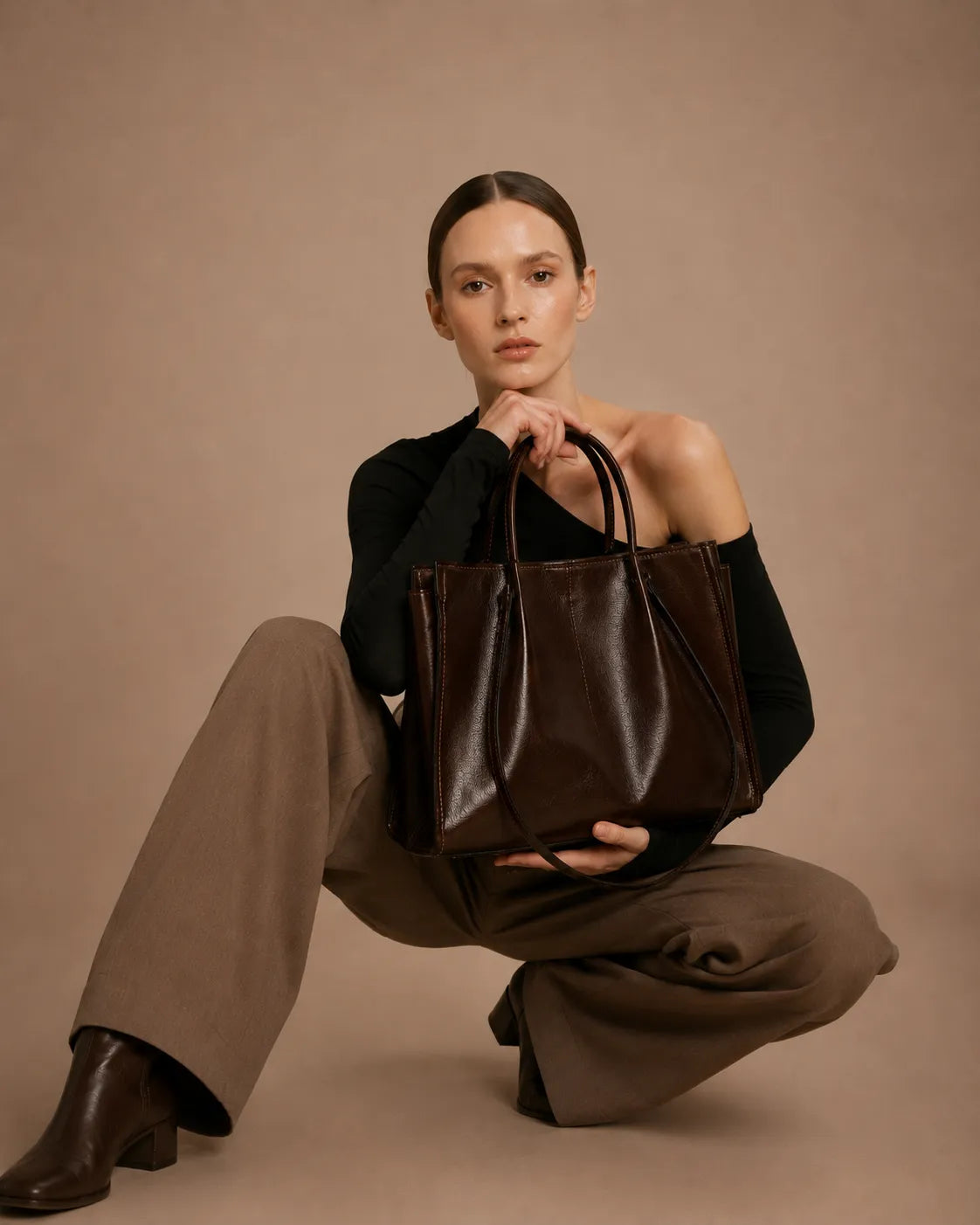 Model holding the Edith Leather Tote Bag in Dark Chocolate genuine leather, styled with tailored trousers and boots in a sophisticated editorial look from The City Edit collection by Malena London.