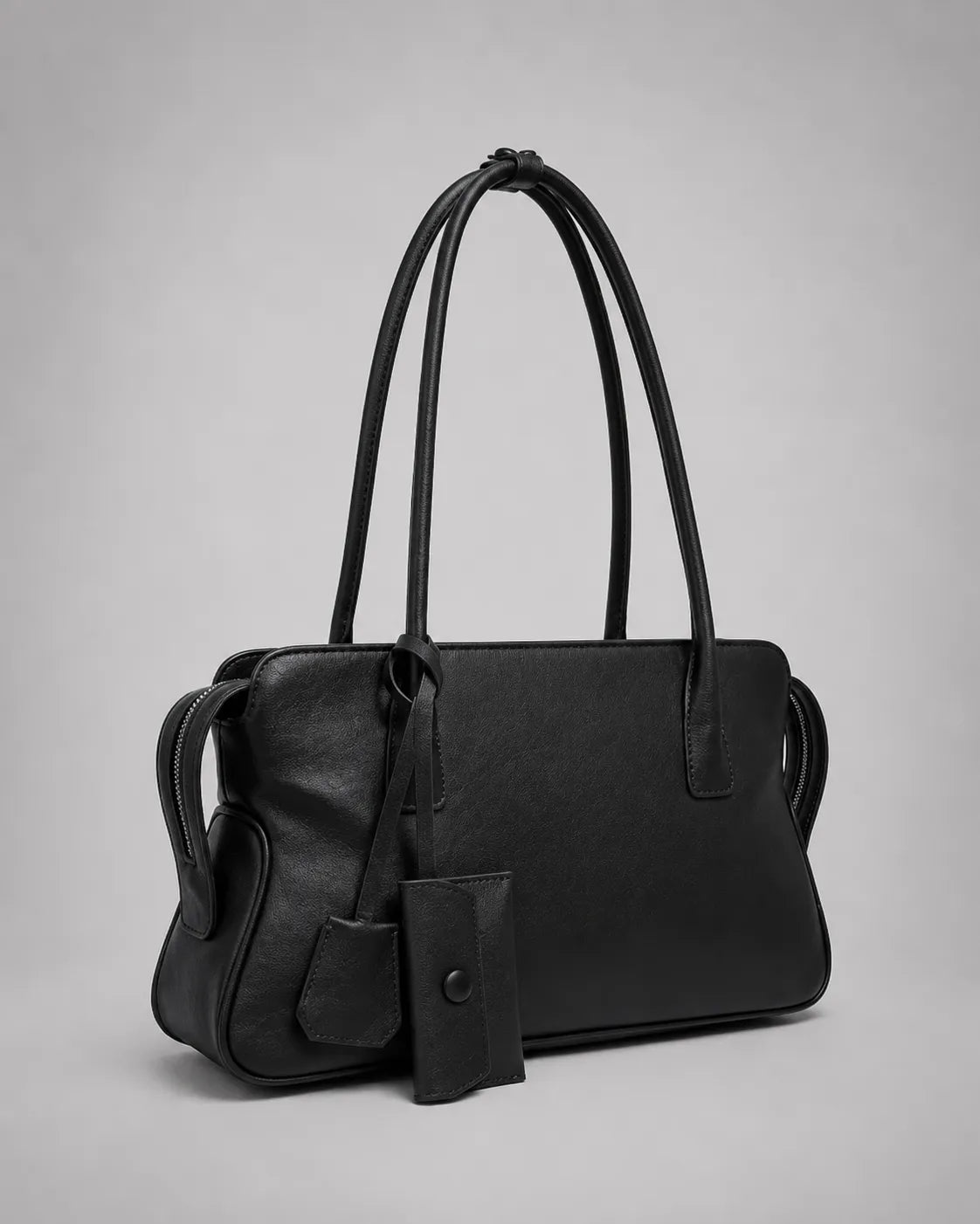 Georgia leather shoulder bag in Black genuine leather shown in a front side angle highlighting the soft structure, elongated shoulder straps, decorative leather charms and timeless everyday design from the Soft Structure collection by Malena London.
