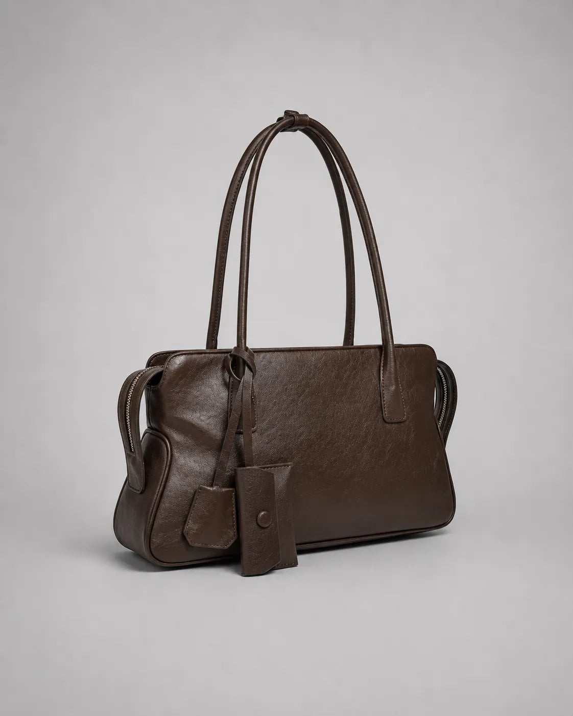 Georgia leather shoulder bag in Dark Chocolate genuine leather shown in a front side angle highlighting the softly structured shape, elongated shoulder straps, leather charms and elegant everyday design from the Soft Structure collection by Malena London.