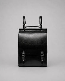 Front view of the Heritage Leather Backpack in Black genuine leather, designed with a structured profile, flap closure, top handle, adjustable shoulder straps and premium metal hardware.