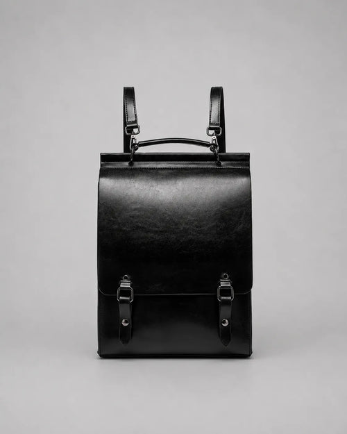 Front view of the Heritage Leather Backpack in Black genuine leather, designed with a structured profile, flap closure, top handle, adjustable shoulder straps and premium metal hardware.