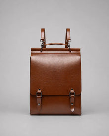 Front view of the Heritage Leather Backpack in Brown genuine leather, featuring a structured silhouette, flap closure, top handle, adjustable shoulder straps and premium hardware.