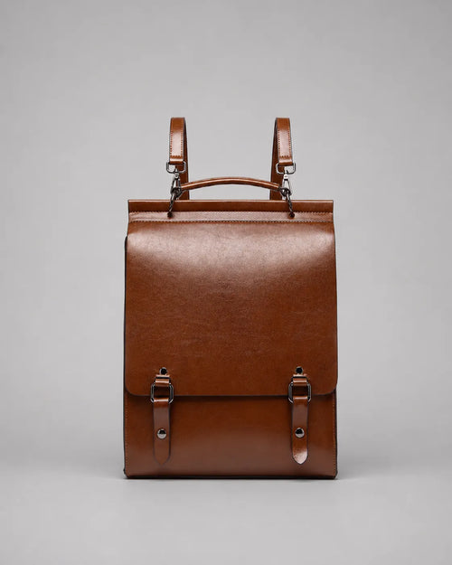Front view of the Heritage Leather Backpack in Brown genuine leather, featuring a structured silhouette, flap closure, top handle, adjustable shoulder straps and premium hardware.