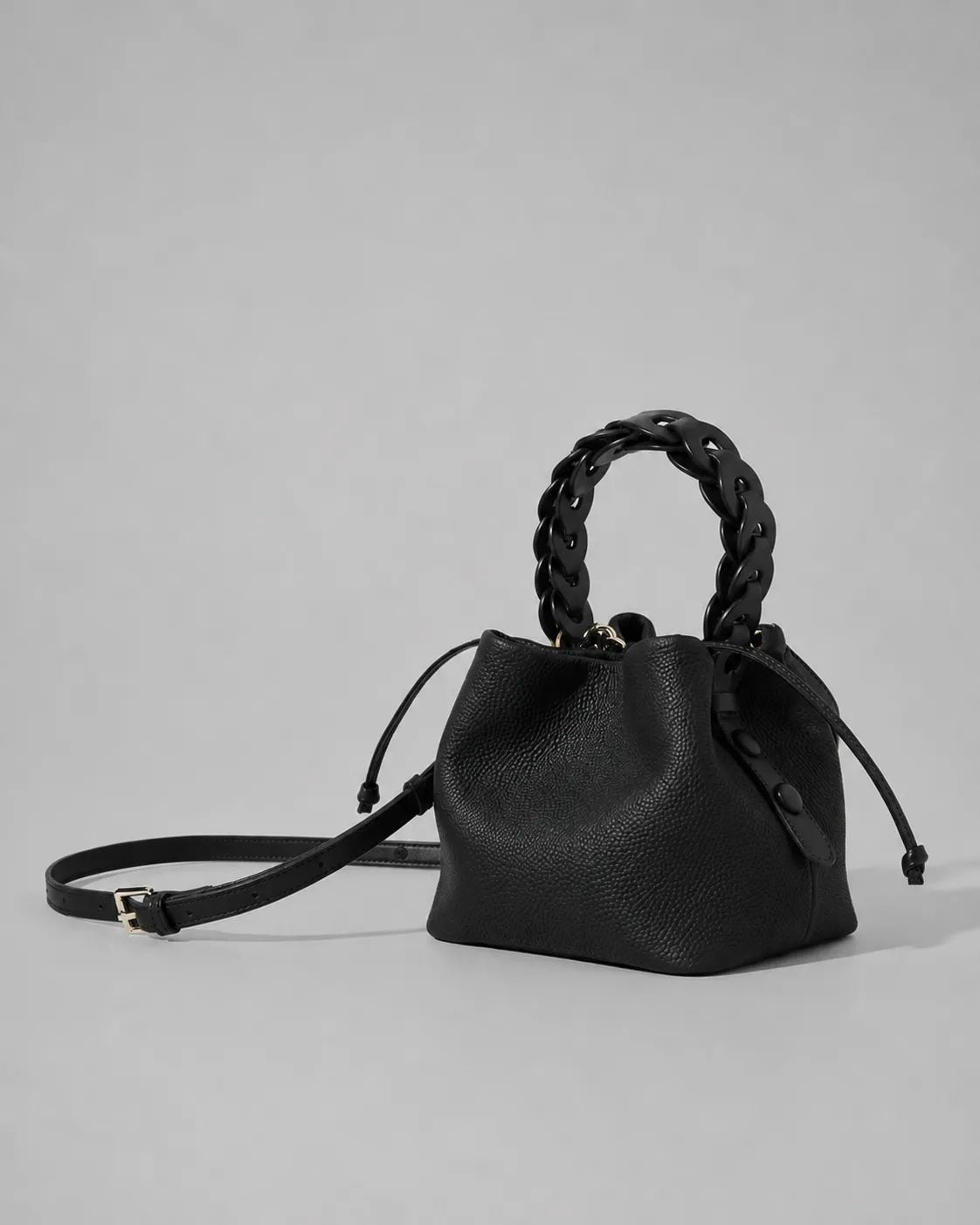 Side angled view of the Léonie genuine leather bucket bag in Black featuring a removable adjustable shoulder strap, braided leather handle, drawstring closure and contemporary bucket silhouette by Malena London.