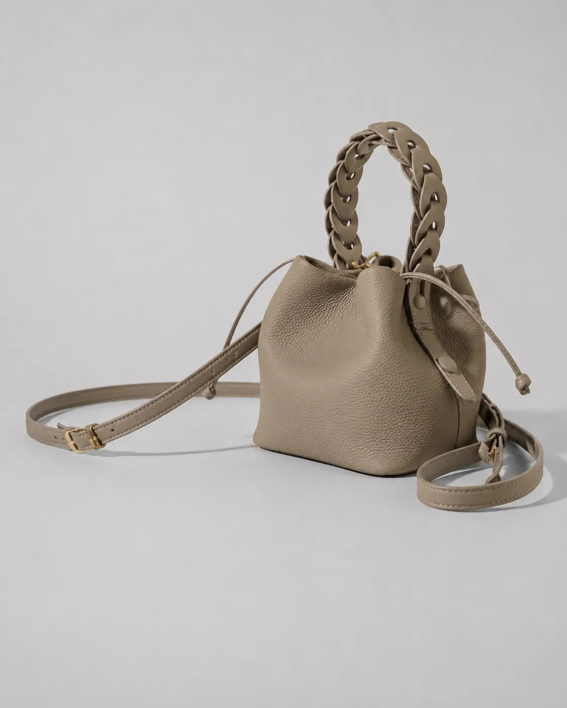 Side angled view of the Léonie genuine leather bucket bag in Elephant Gray featuring a removable shoulder strap, braided leather handle and softly structured bucket shape by Malena London.