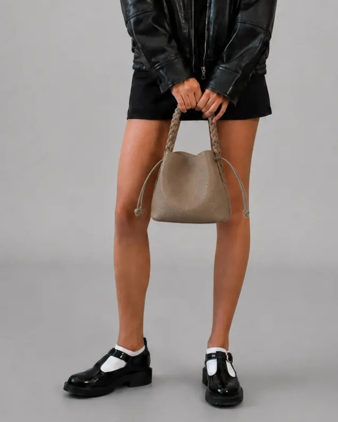 Woman holding the Malena London Léonie genuine leather bucket bag in taupe. Elegant designer leather bucket bag with braided top handle and timeless everyday style.