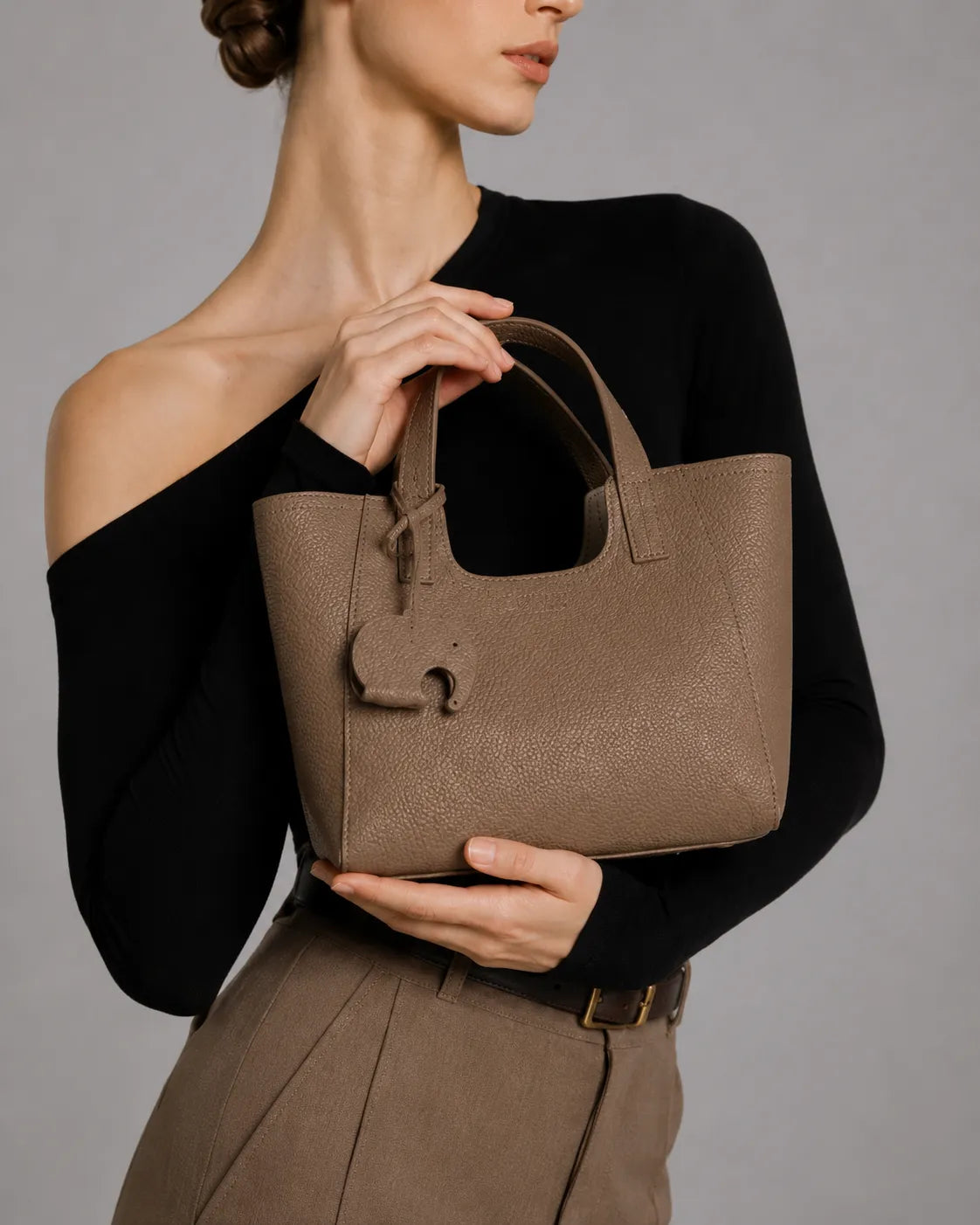Woman holding the Louise genuine leather mini tote bag in Elephant Gray. Elegant structured leather handbag with top handles, compact silhouette and timeless design for everyday wear, work and city outings.